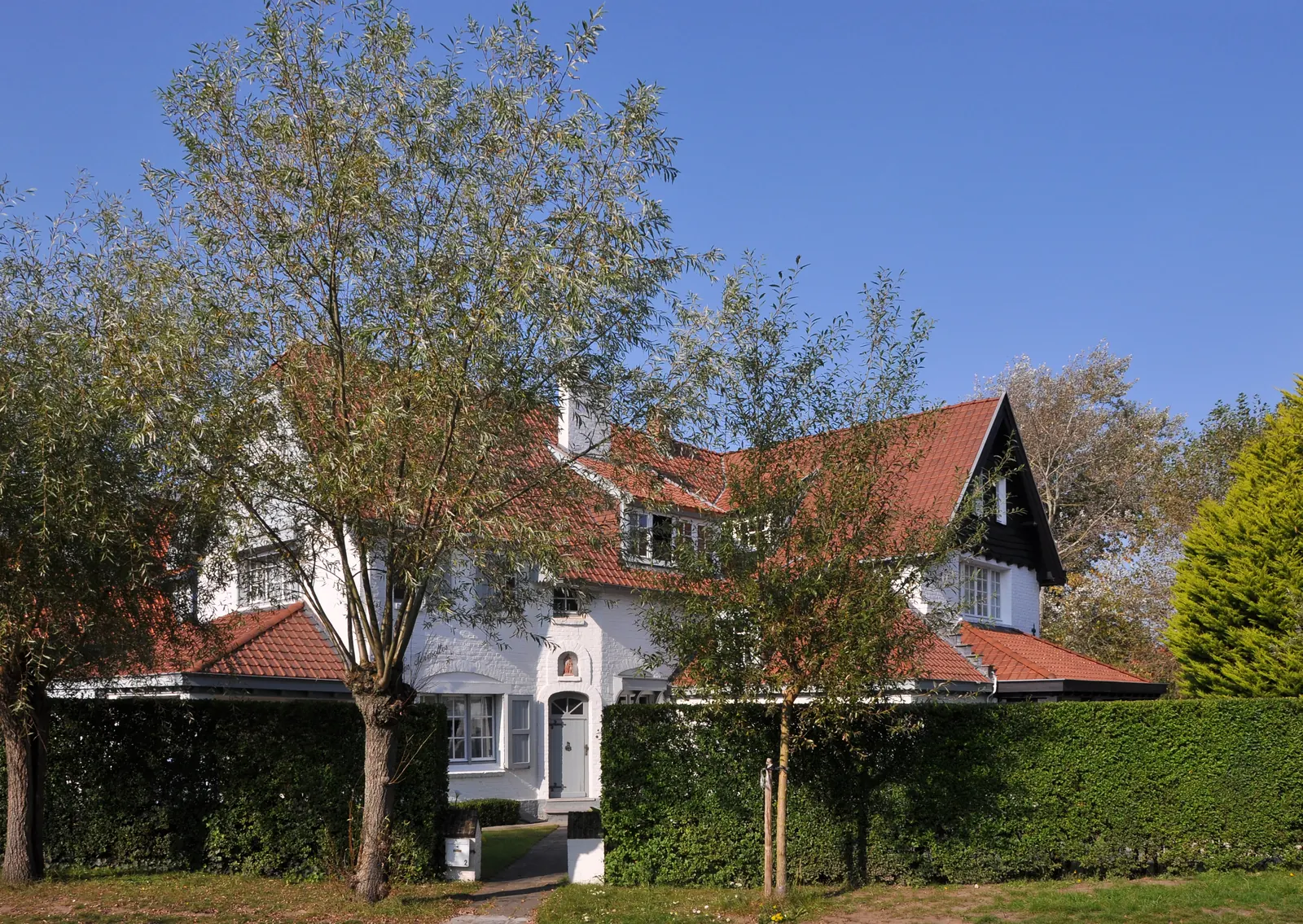 Wäiss Villa mat rouden Zillendiecher hannert enger Heck an der Concessie zu De Haan