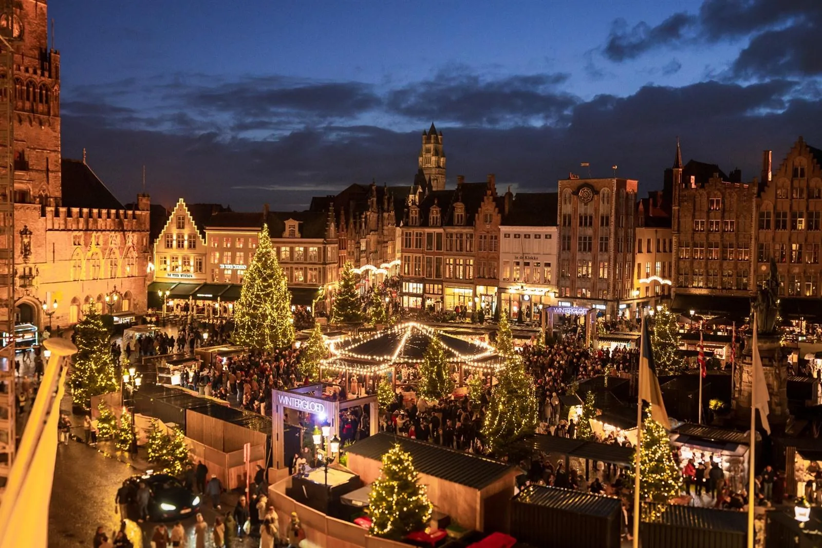 Weihnachtsmarkt auf dem Markt in Brügge von oben, mit beleuchteten Ständen und Weihnachtsbäumen am Abend