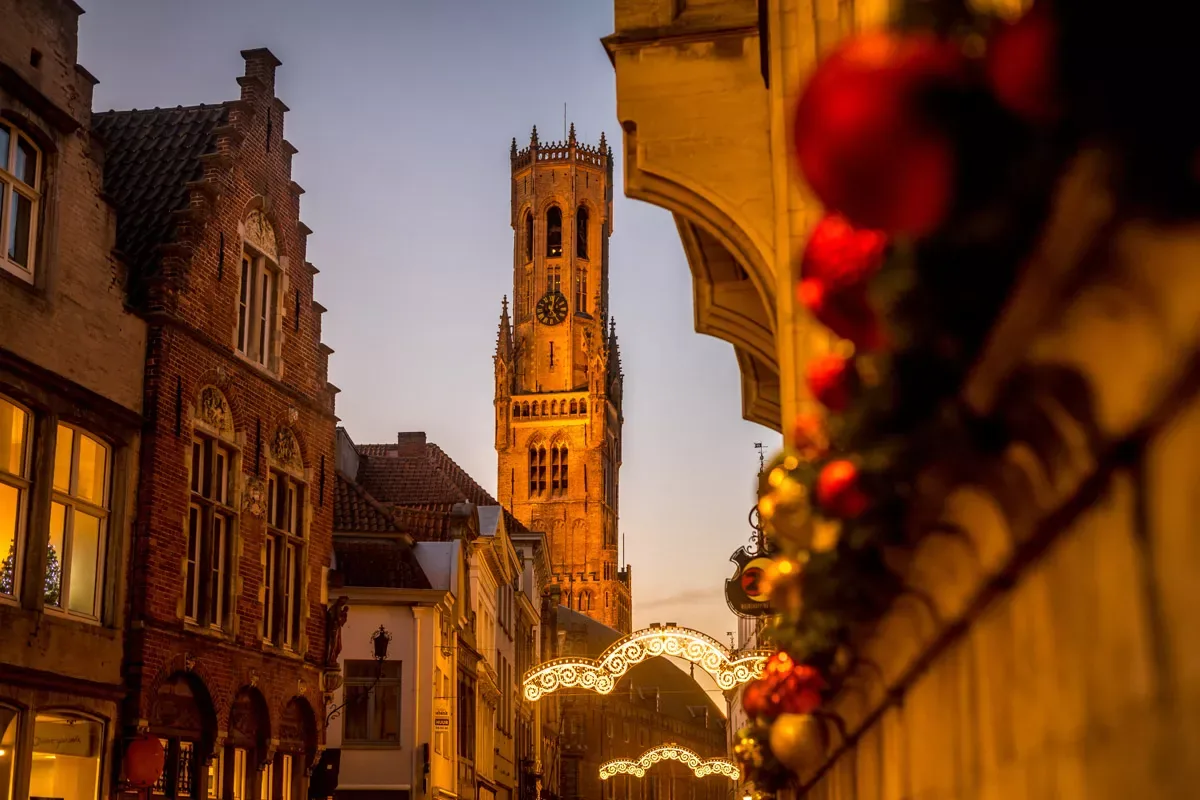 Beleuchtete Winterstraße in Brügge in Richtung Belfried, mit Weihnachtskugeln im Vordergrund