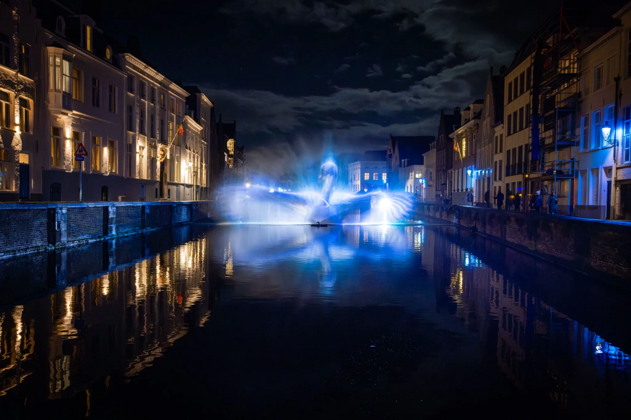Lichtinstallation über einer Brügger Gracht bei Nacht, gespiegelt im blauen Wasser