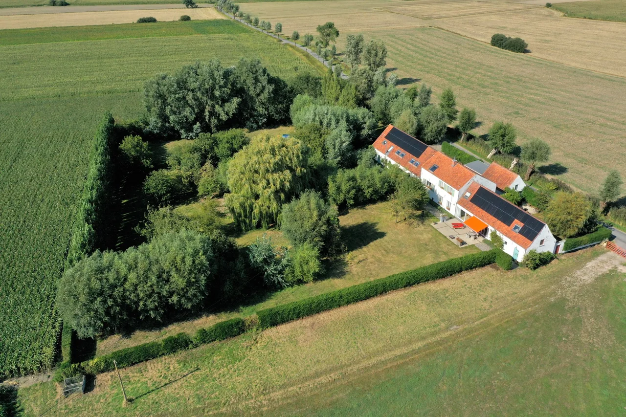 Echt Loftbild vu Polderlicht: de wäisse Bauerenhaff mat orangen Diech a Solarpanneauen tëscht Beem, Gaart a Polderfelder